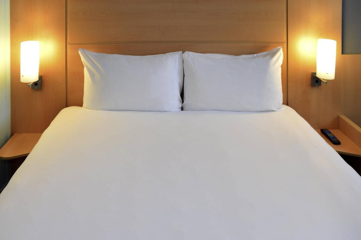 A neatly made bed with white linens and two bedside lamps on wooden nightstands.