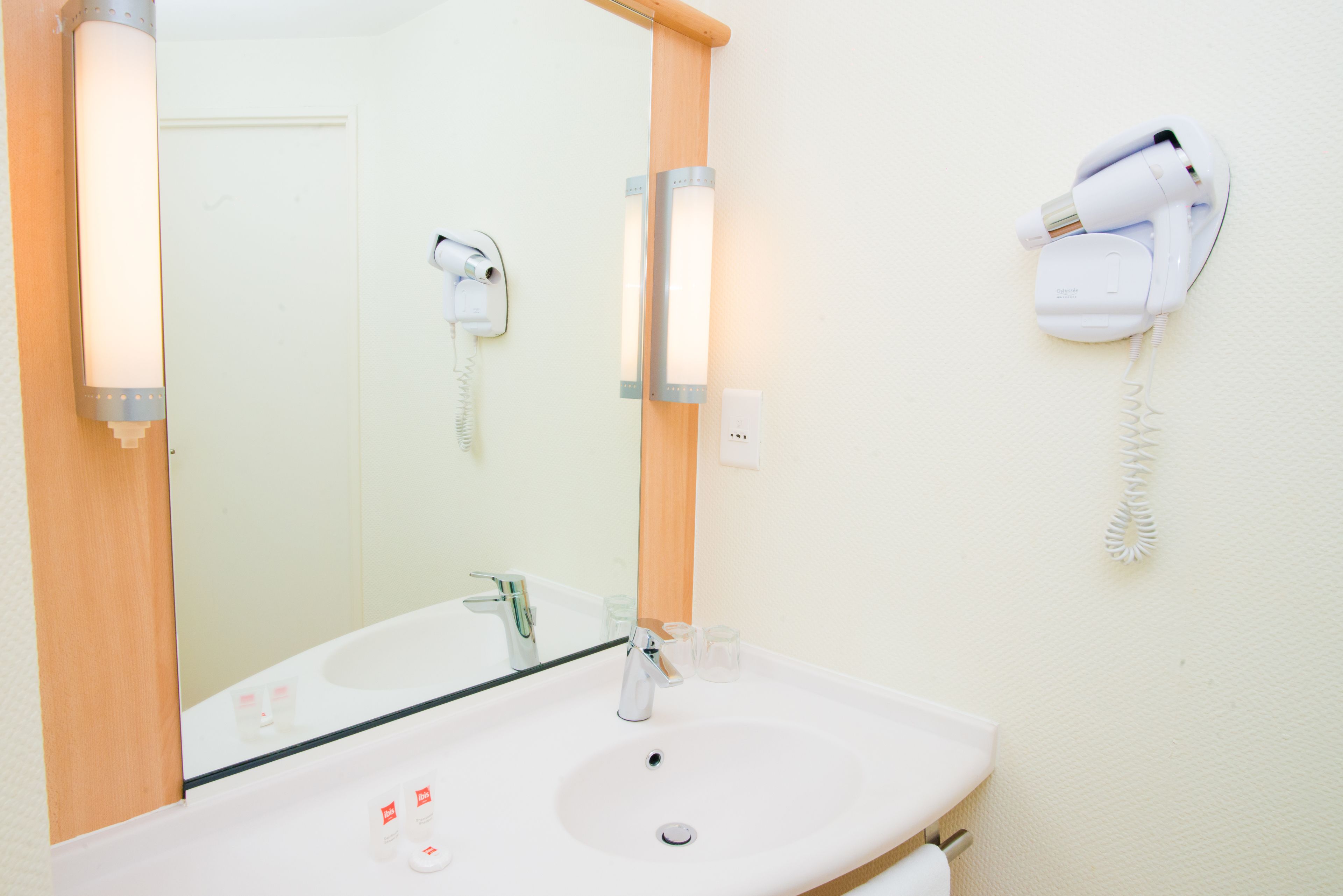 A bathroom with a white sink, a mirror, a hairdryer, and a phone on the wall.