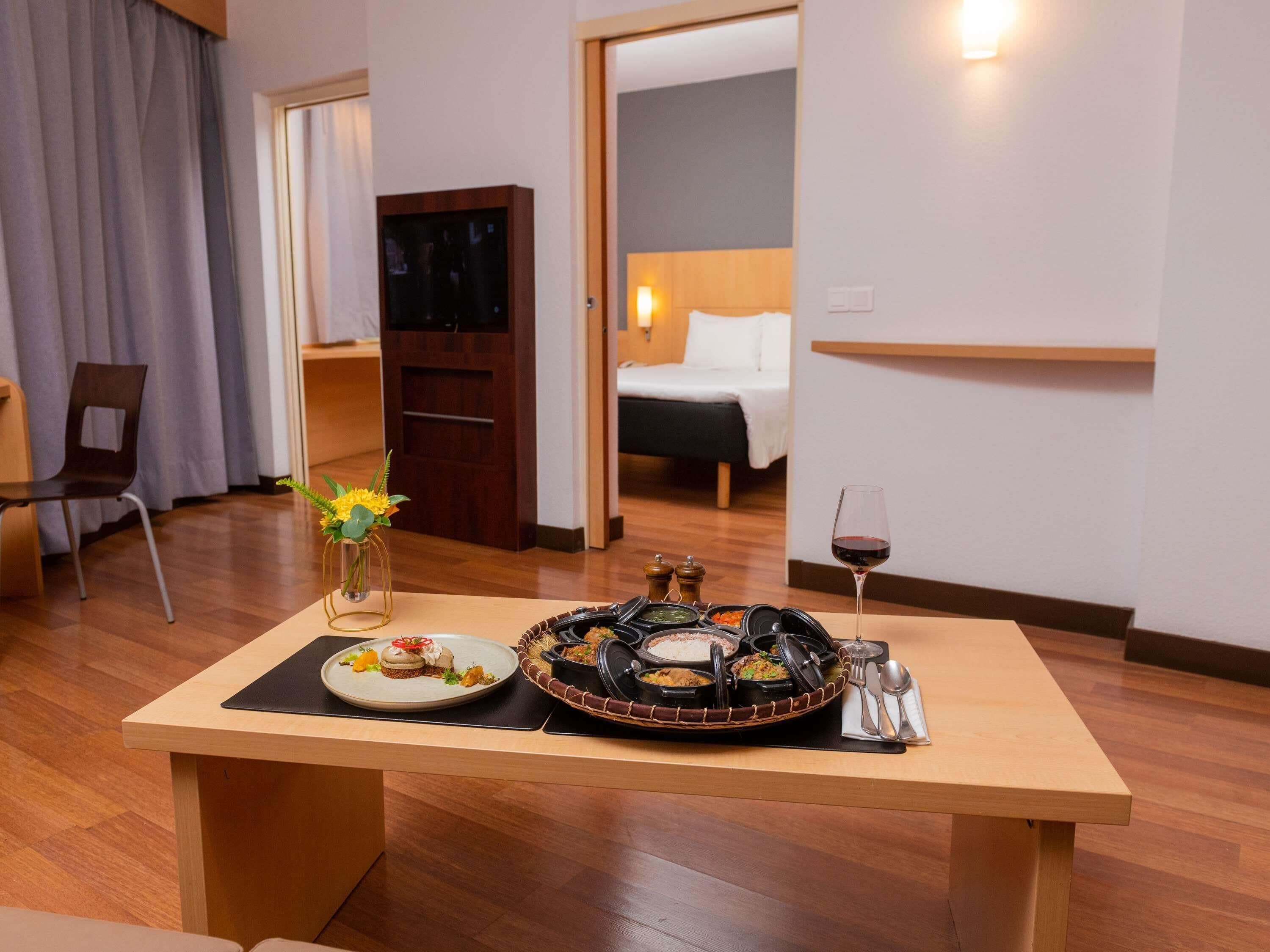 Une chambre d’hôtel avec une table à manger dressée, comprenant des assiettes, un vase de fleurs et un verre à vin.