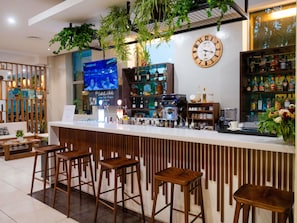 Zona de bar con taburetes de madera, un reloj y estantes con botellas.
