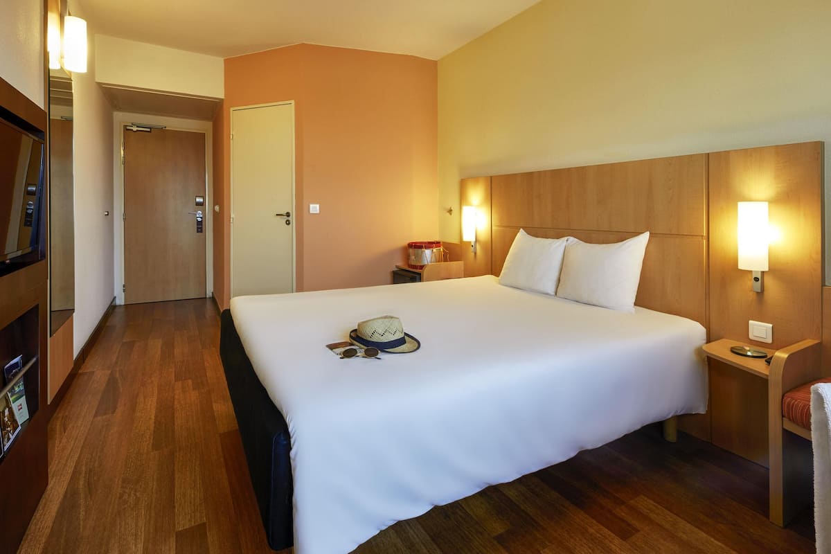 A hotel room with a large bed, wooden headboard, bedside tables, and a television.