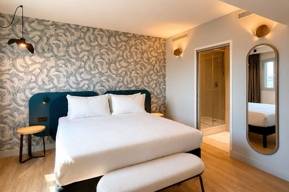 A bedroom with a bed, bedside tables, a mirror, and a shower area.