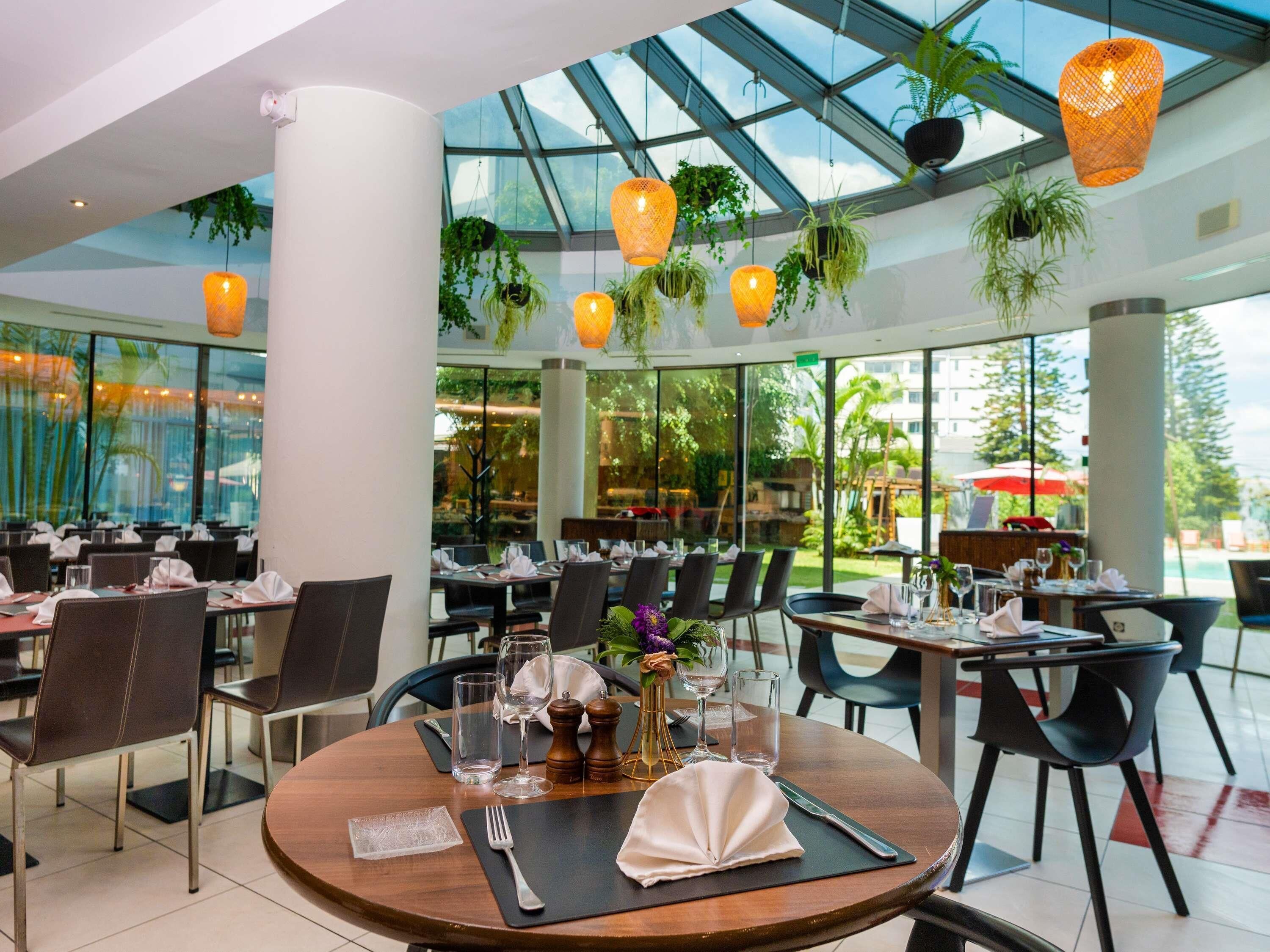 Un restaurant avec des tables rondes, des chaises noires et des plantes suspendues.