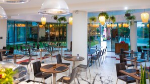 A modern restaurant with glass walls, multiple dining areas, and hanging pendant lights. - ibis Antananarivo Ankorondrano (Antananarivo)