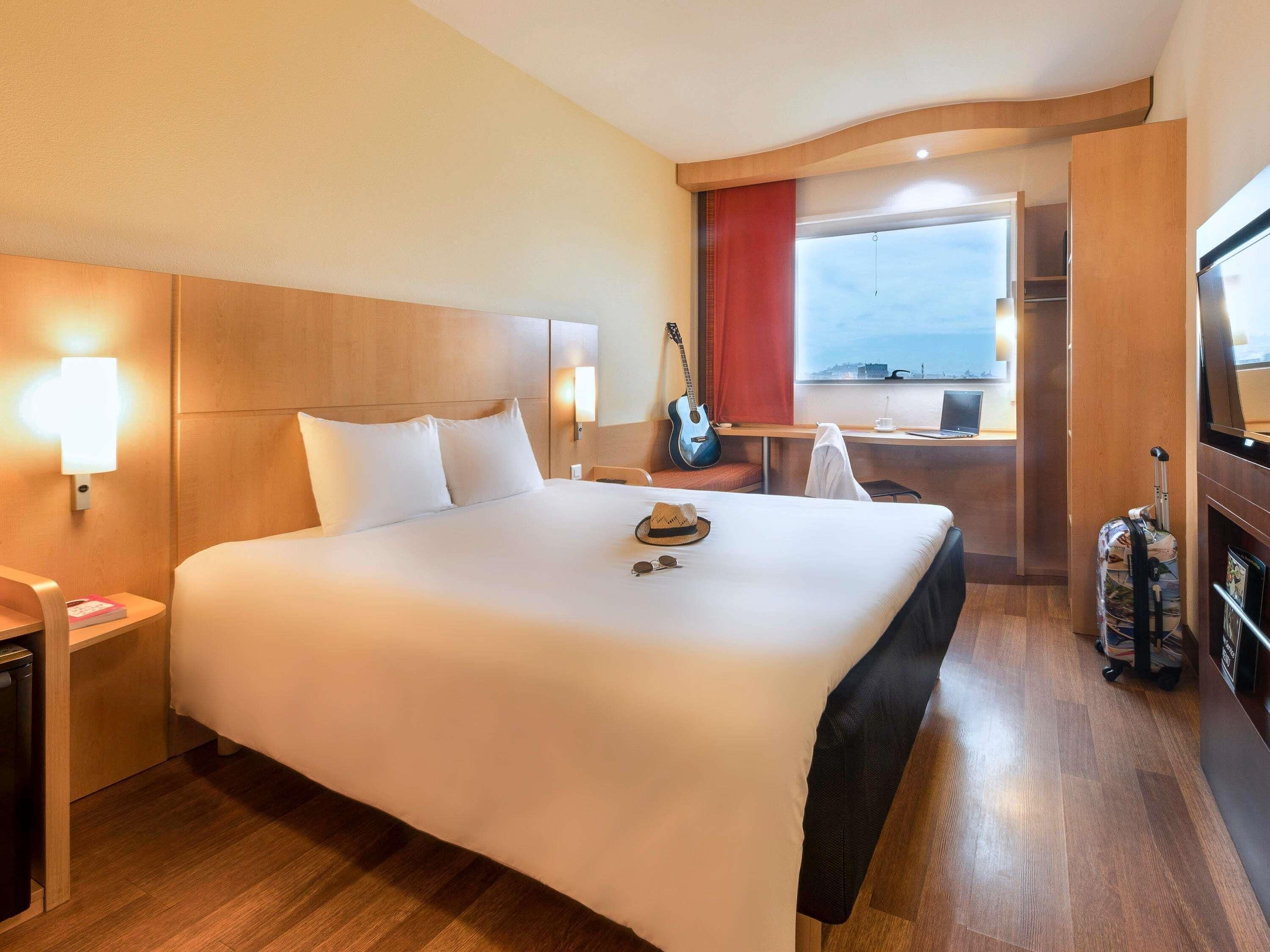 Une chambre d’hôtel avec un grand lit, des lampes de chevet, un bureau avec un ordinateur portable, une guitare et une vue sur la mer.