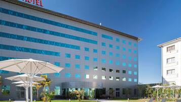 Experience the sleek exterior of ibis Hotel, featuring a flat facade and a spacious pool area with lounge chairs.