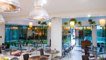A modern restaurant with glass walls, multiple dining tables, and hanging pendant lights.