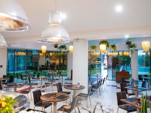A modern restaurant with glass walls, multiple dining tables, and hanging pendant lights. - ibis Antananarivo Ankorondrano (Antananarivo)