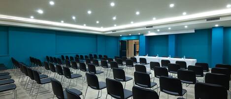 A conference room with rows of black chairs, a white table with a water dispenser, and blue walls.