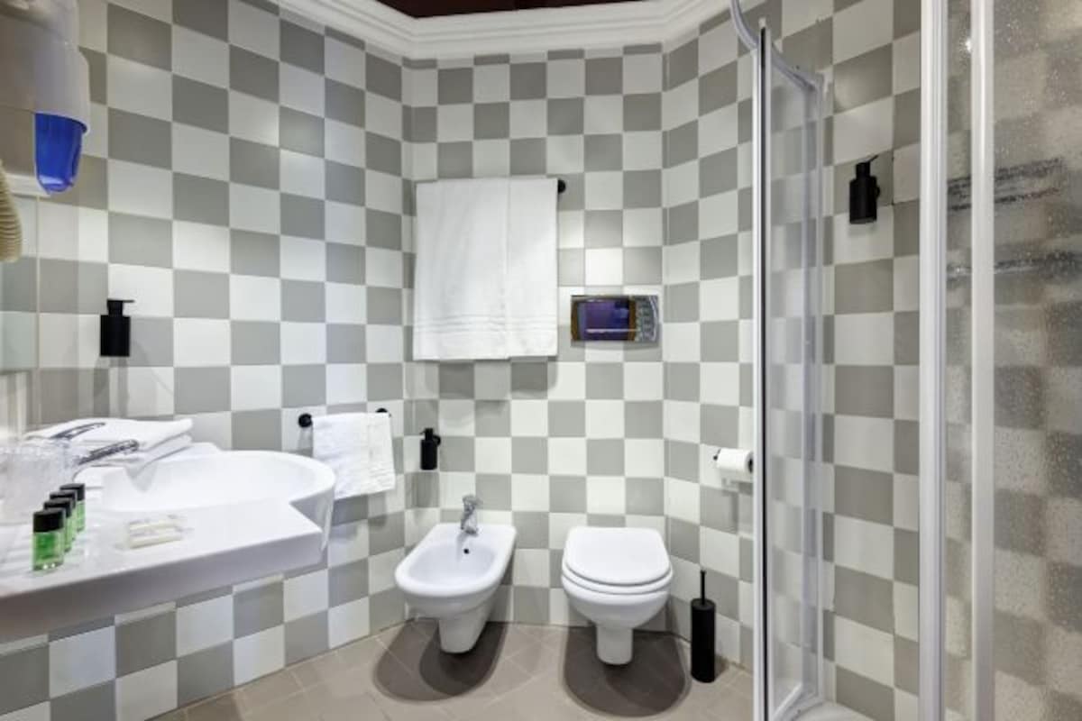 A bathroom with a checkered tile wall, a sink, a bidet, and a toilet.