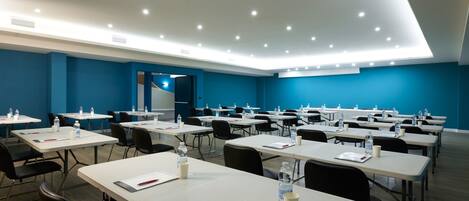 Un salón de conferencias con mesas, sillas y botellas de agua.