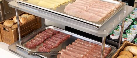 A buffet with various food items including sliced meats, cheeses, and bread.