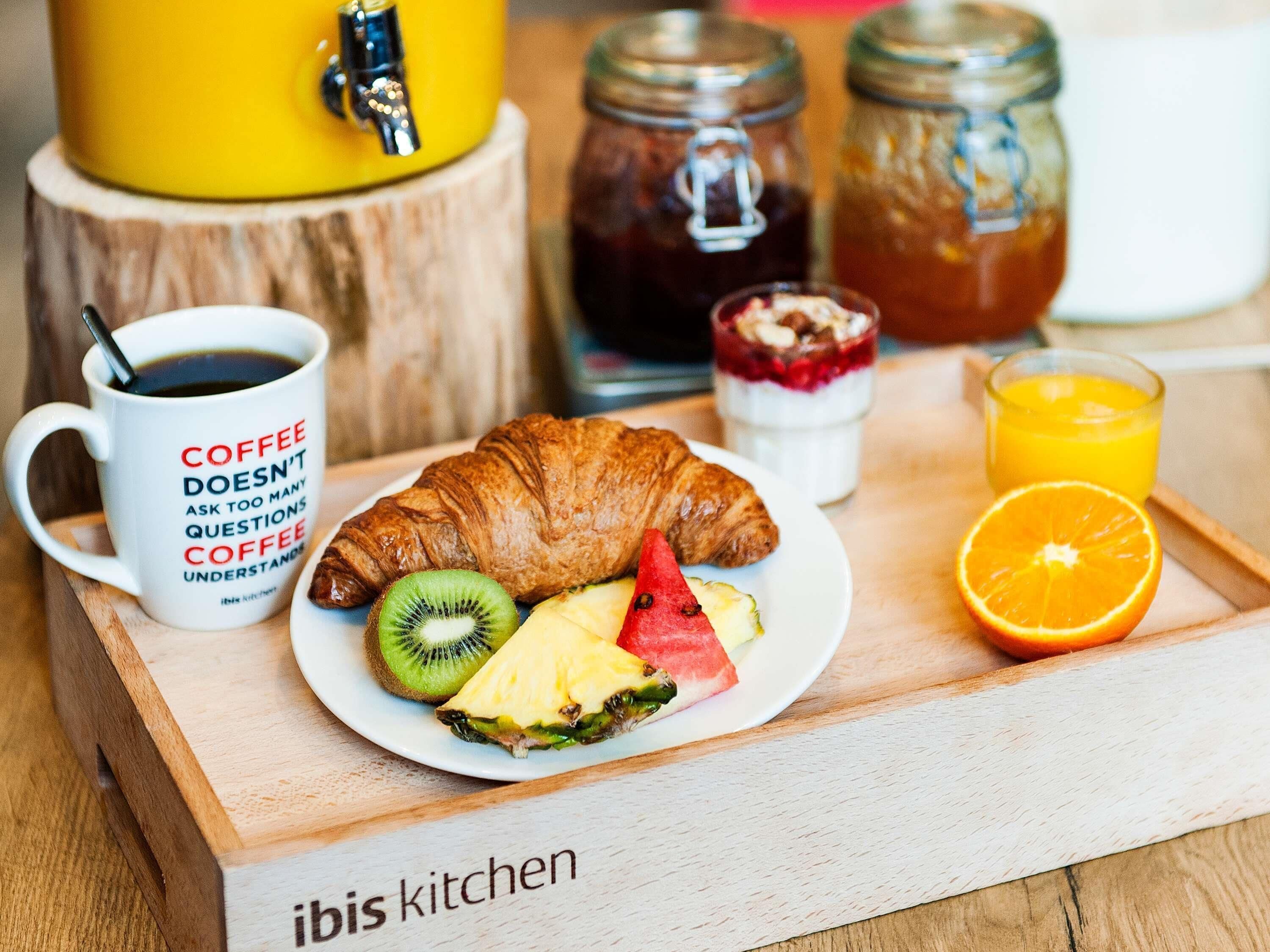 Bandeja de desayuno con un croissant, kiwi, piña, sandía, zumo de naranja, café y mermelada.
