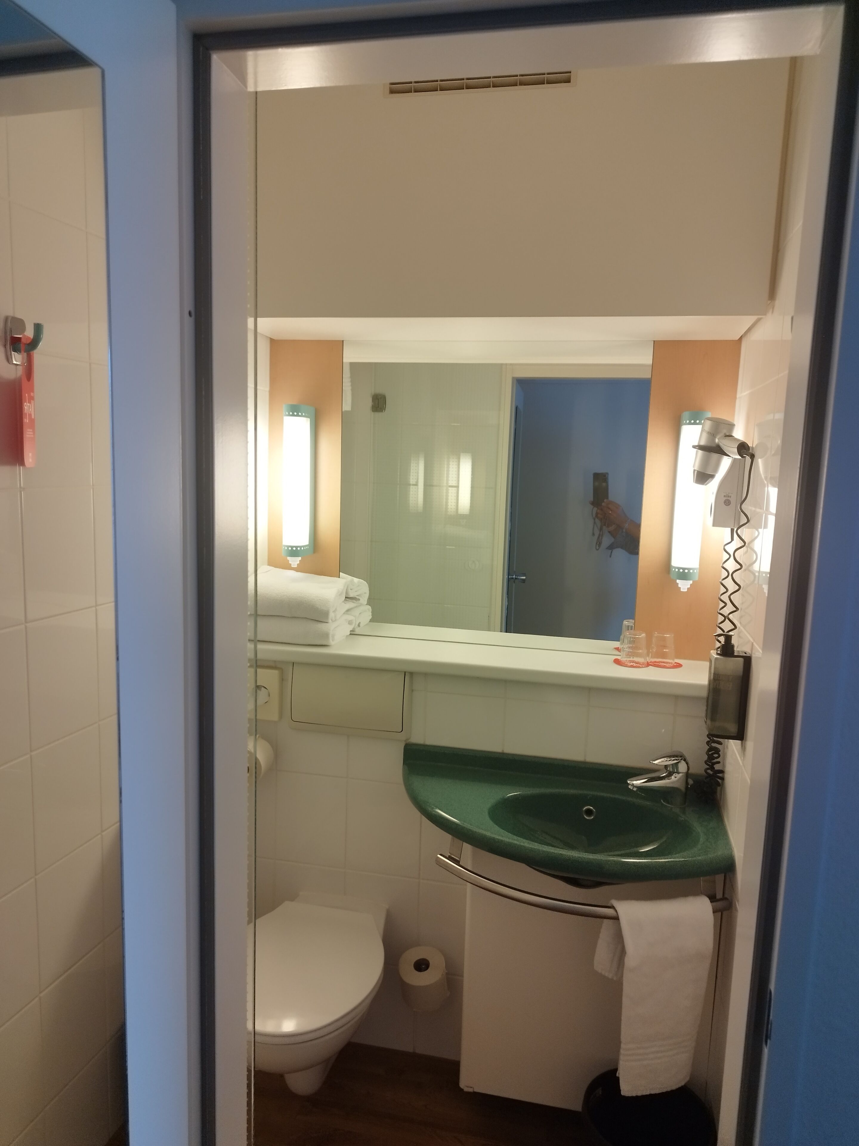 A compact bathroom with a white toilet, a green sink, and a mirror above it.