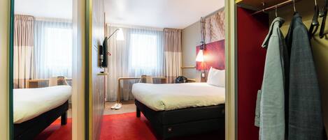 A hotel room with two beds, a red carpet, a mirror, a coat rack, and a television.