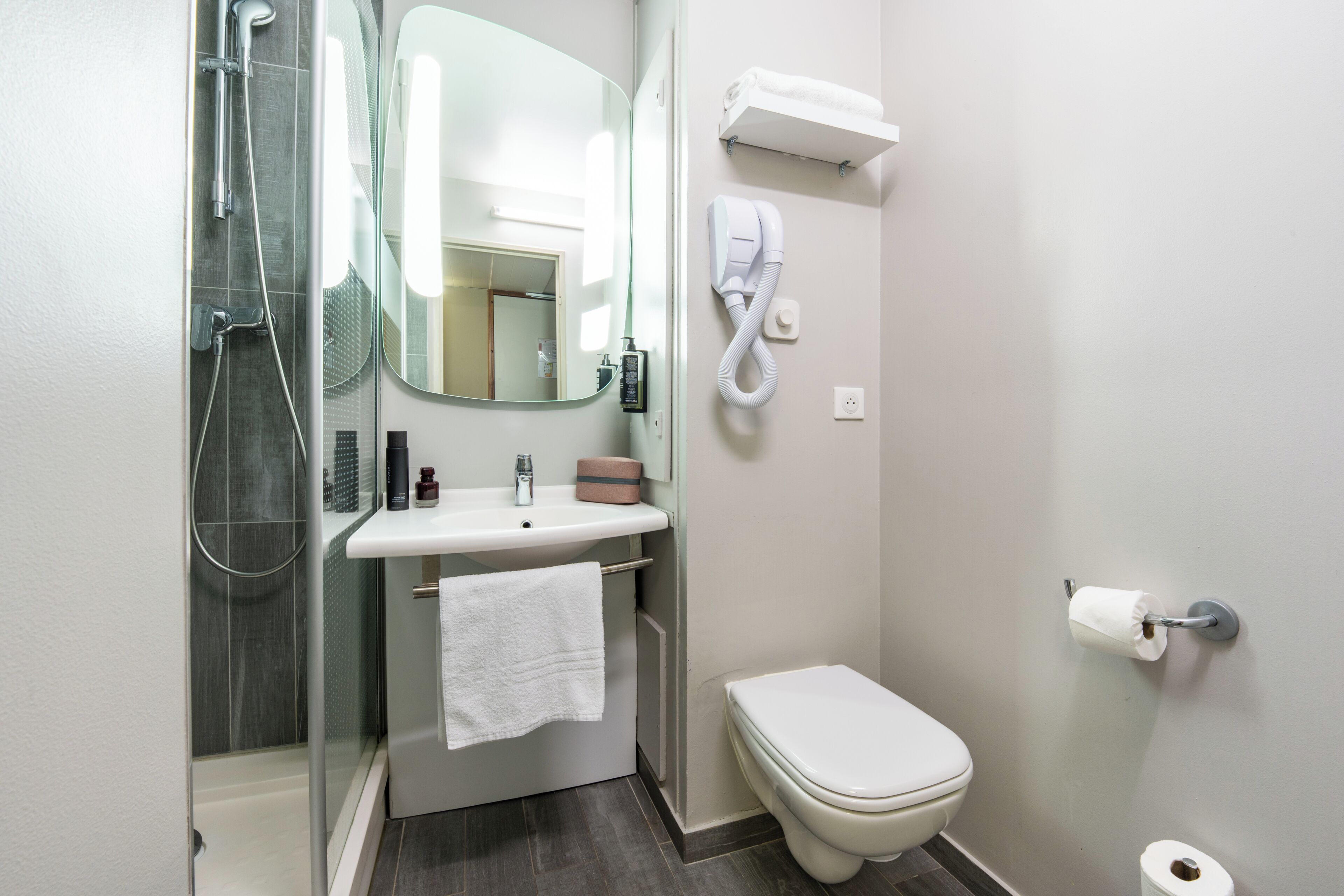 A bathroom with a shower, sink, toilet, and a mirror.