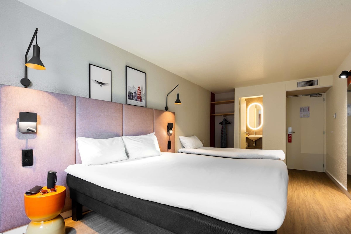 A hotel room with a large bed, bedside lamps, a wall-mounted phone, and a mirror.