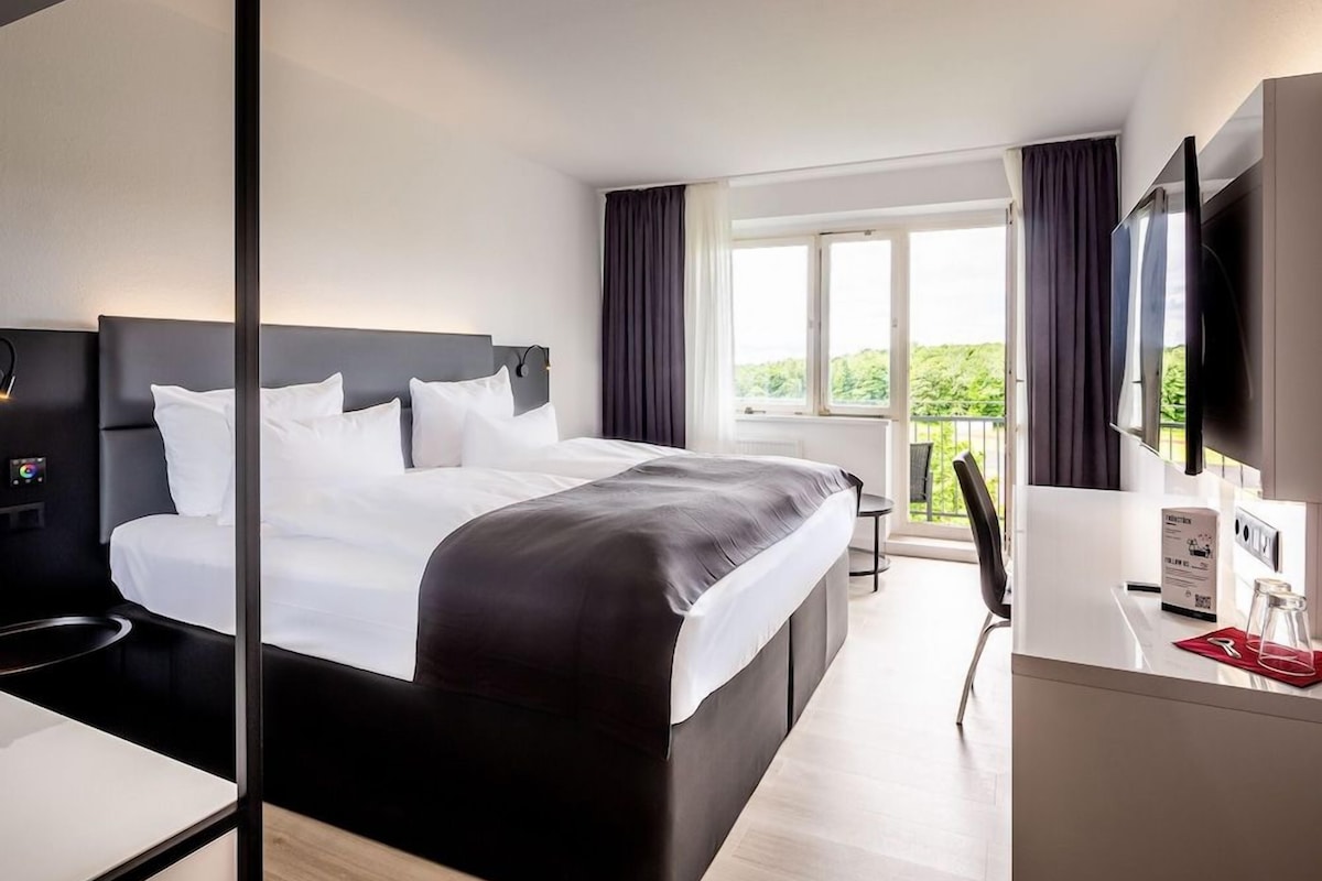 A modern hotel room with a large bed, a desk, a chair, and a television.