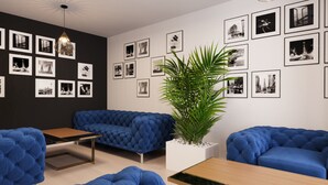 A modern lounge area with a dark wall, a blue sofa, a wooden table, and a potted plant. - DORMERO Hotel Weimar (Weimar)