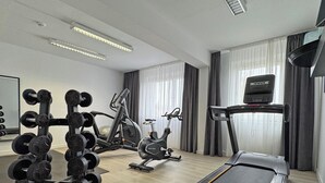 A modern home gym with a treadmill, elliptical, and weight bench. - DORMERO Hotel Weimar (Weimar)