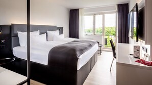 A modern hotel room with a large bed, a desk, and a balcony with a view. - DORMERO Hotel Weimar (Weimar)