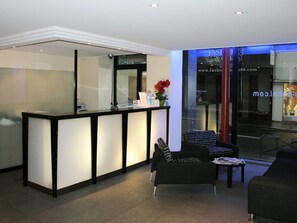 Una zona de recepción moderna con un mostrador negro, un sofá negro y una mampara de cristal.