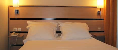 A hotel room with a large bed, two bedside lamps, a phone, and a wooden headboard.