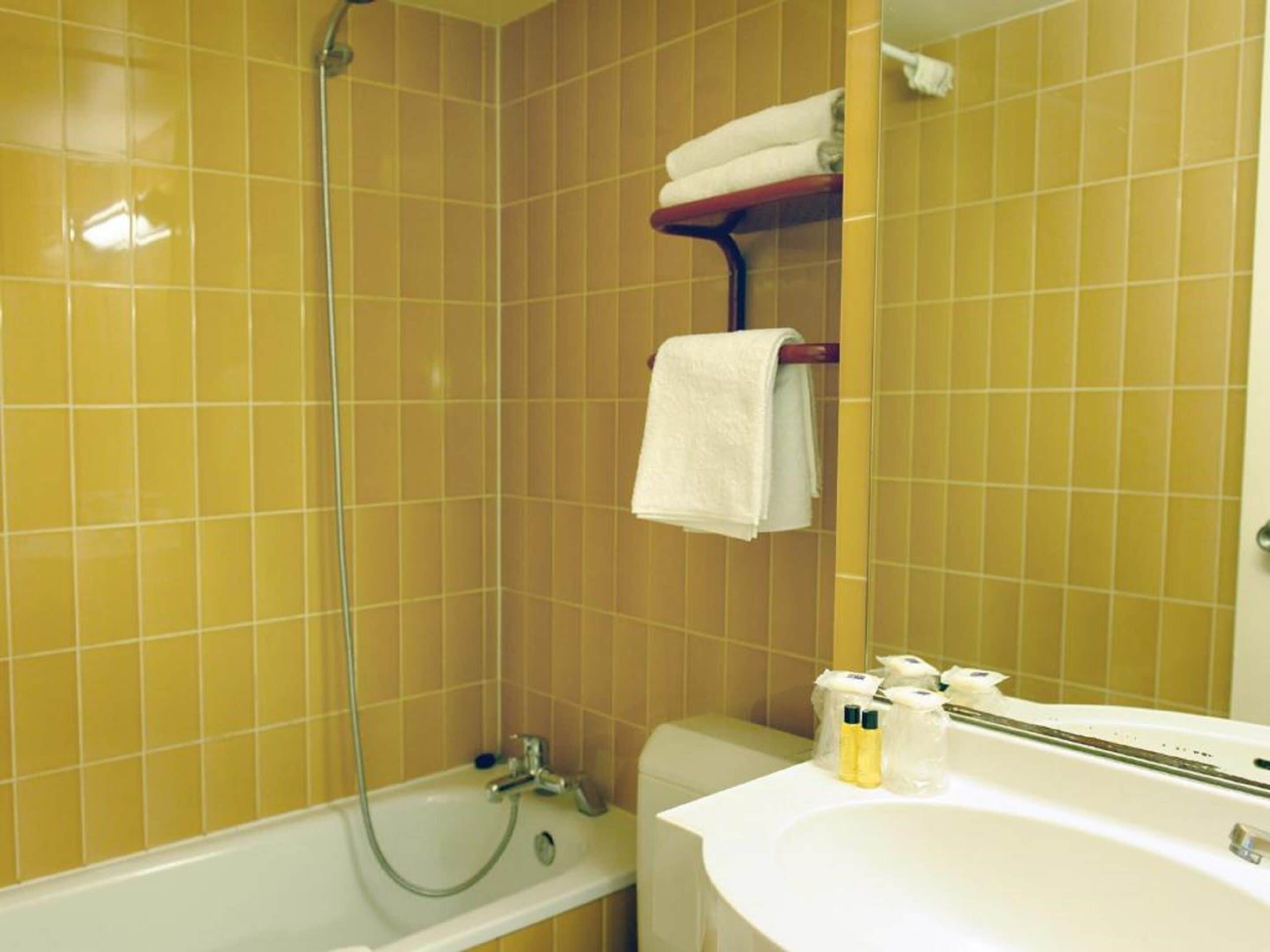 Une salle de bain avec des carreaux jaunes, une baignoire, une douche et un lavabo avec des articles de toilette.