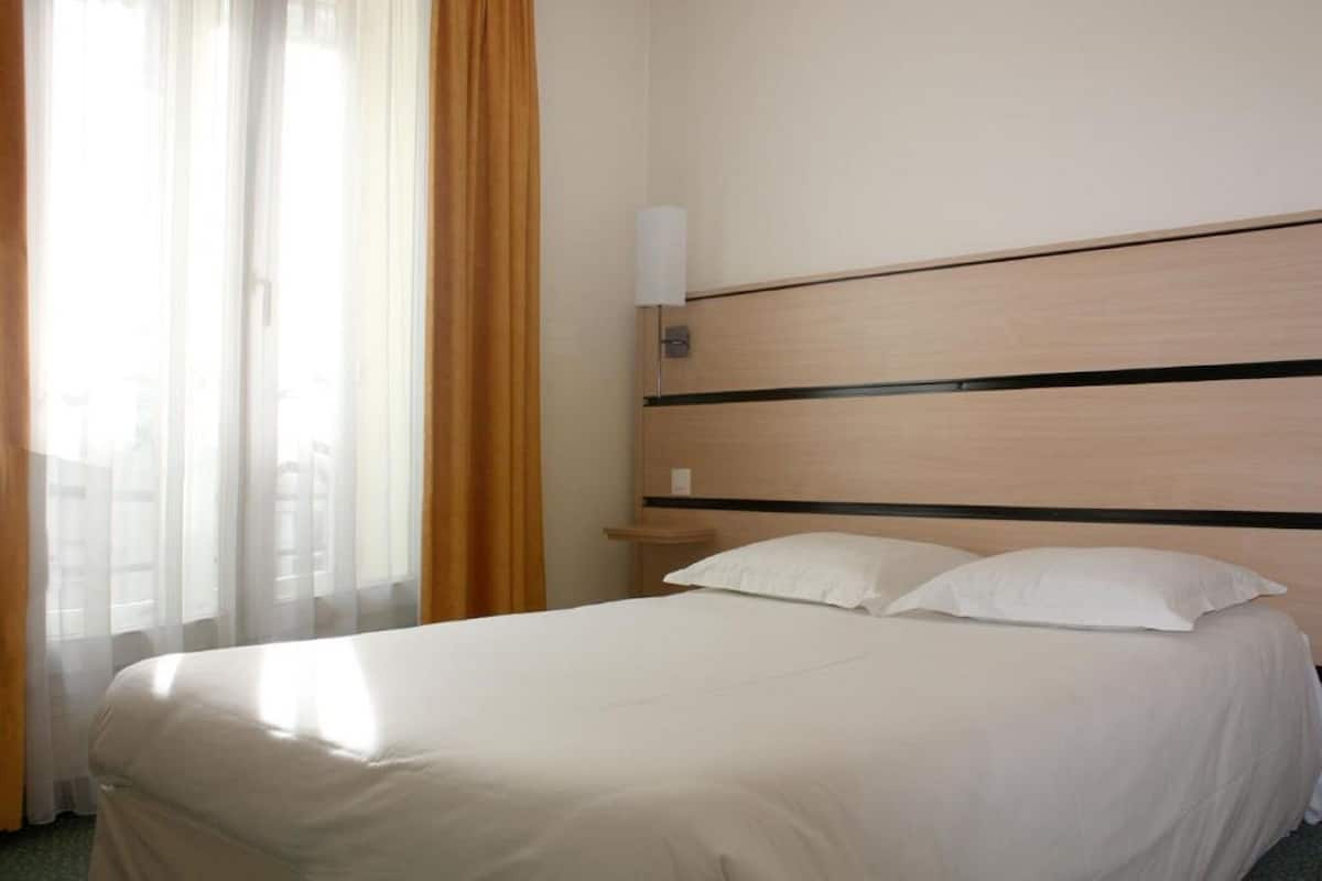 A hotel room with a bed, a nightstand, and a lamp.