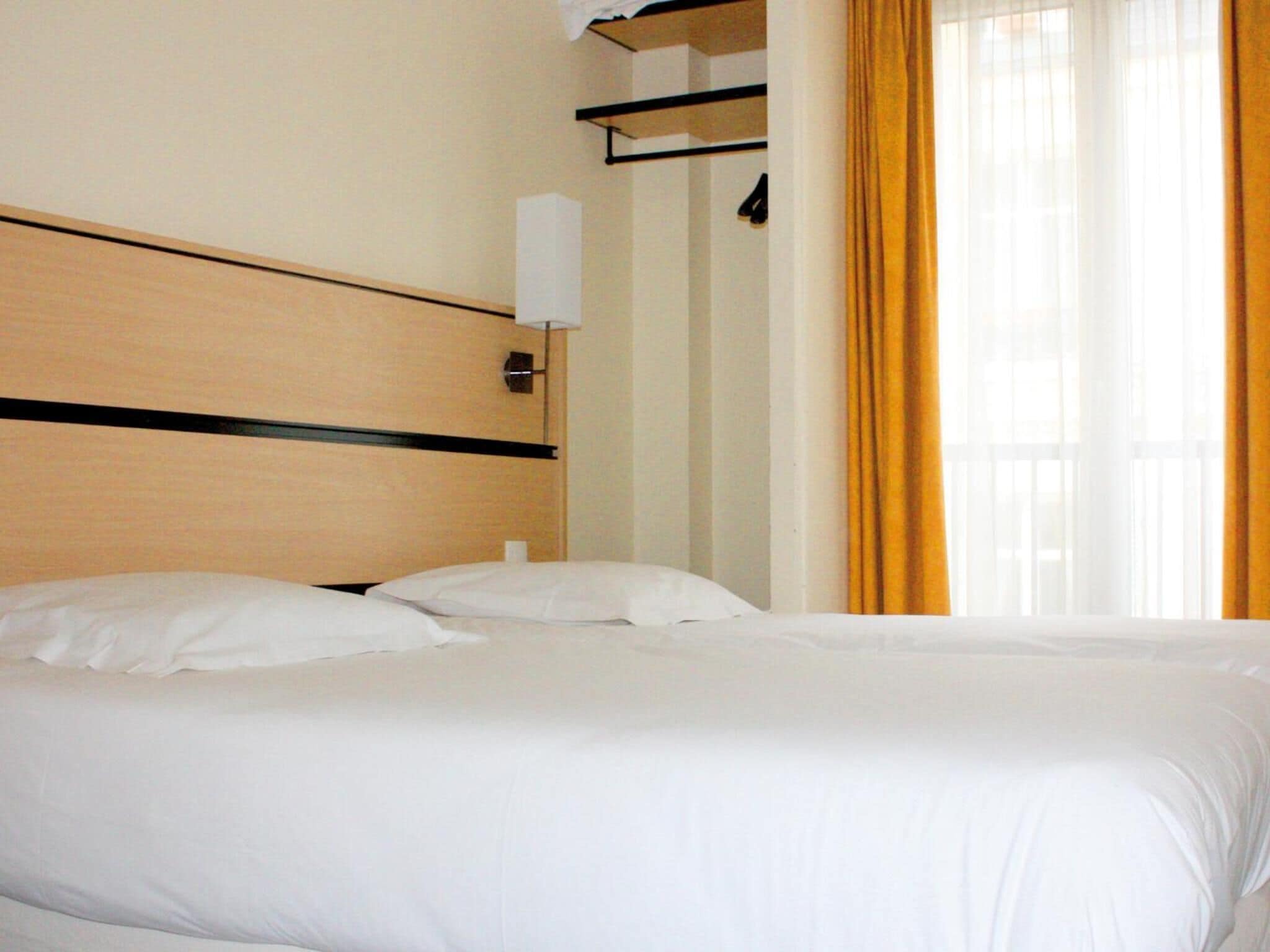 Habitació d'hotel amb un llit gran, un capçal de llit, una tauleta de nit i una finestra amb cortines.