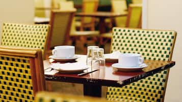 Una mesa de comedor dispuesta con tazas, platos y cubiertos blancos, rodeada de sillas a cuadros.