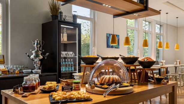 A buffet setup with various food items, a coffee station, and a decorative cabinet. - Vienna House Easy by Wyndham Amberg (Amberg)