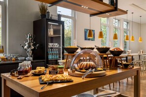 A buffet setup with various food items, a coffee station, and a decorative cabinet. - Vienna House Easy by Wyndham Amberg (Amberg)