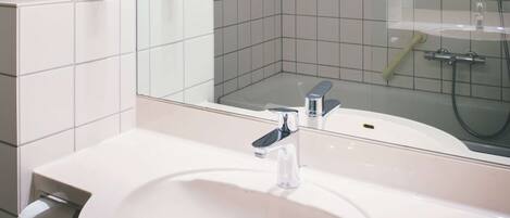 A bathroom with a white sink, a mirror, and a shower area.