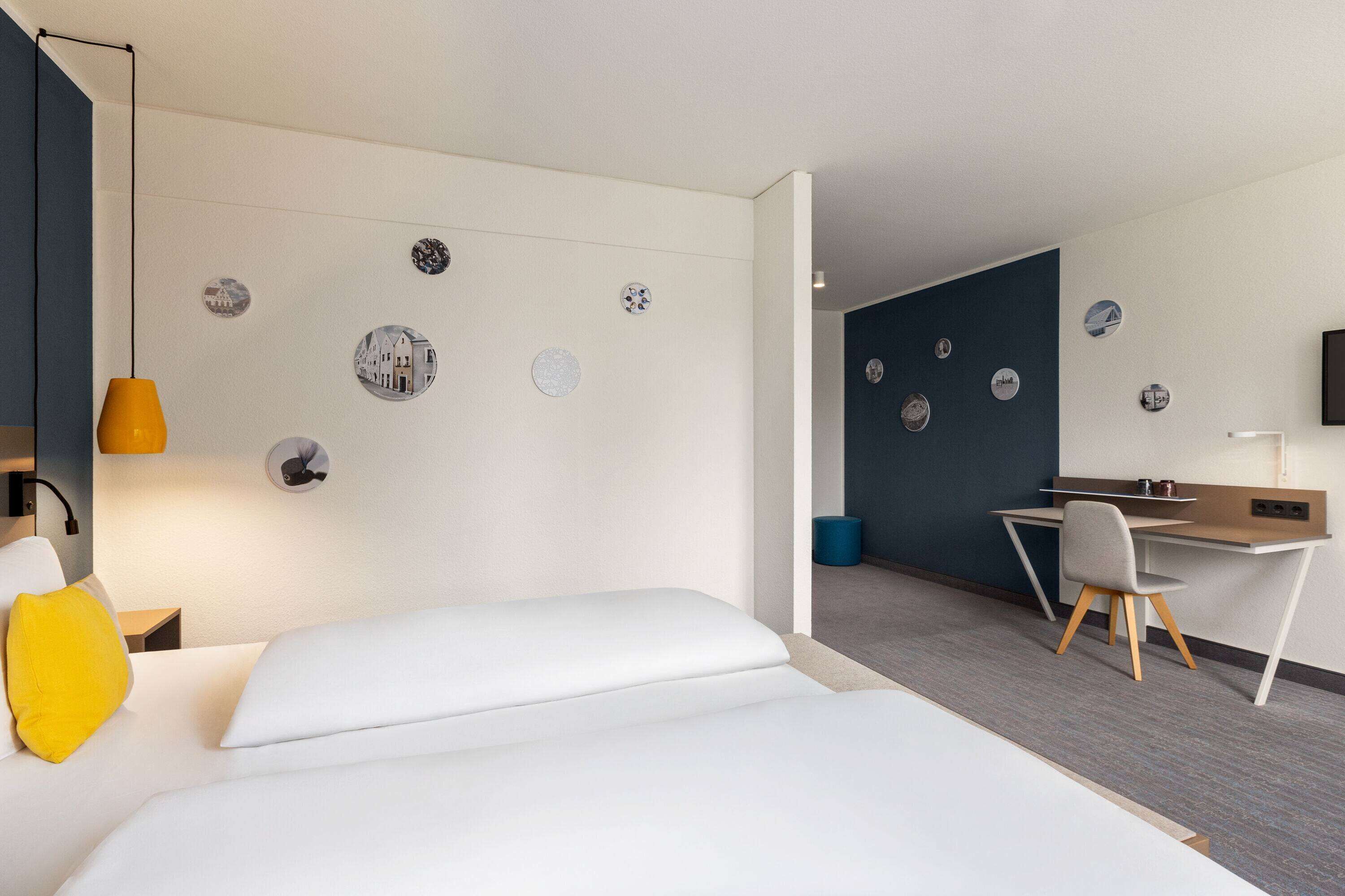 Une chambre d’hôtel moderne équipée d’un lit, d’un bureau et d’une chaise, d’une lampe de bureau et de décorations murales.