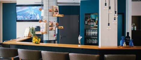 A modern bar area with a wooden counter, bar stools, a television screen, and a decorative metal rack.