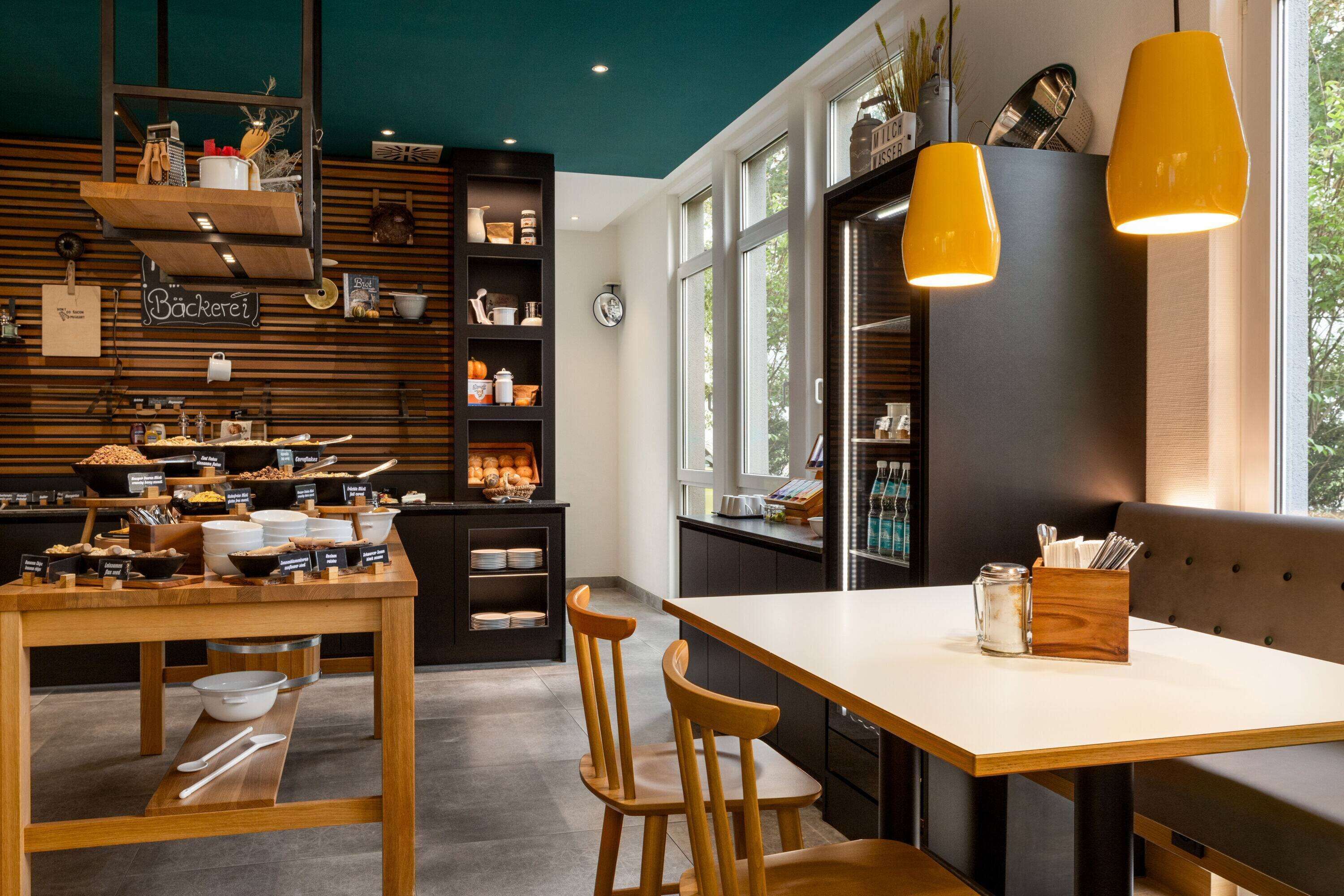 Une cuisine moderne avec des étagères en bois, une table à manger et deux lampes suspendues.
