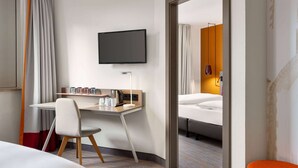 A hotel room with a bed, a desk with a chair, a TV, and a window with curtains. - Vienna House Easy by Wyndham Amberg (Amberg)