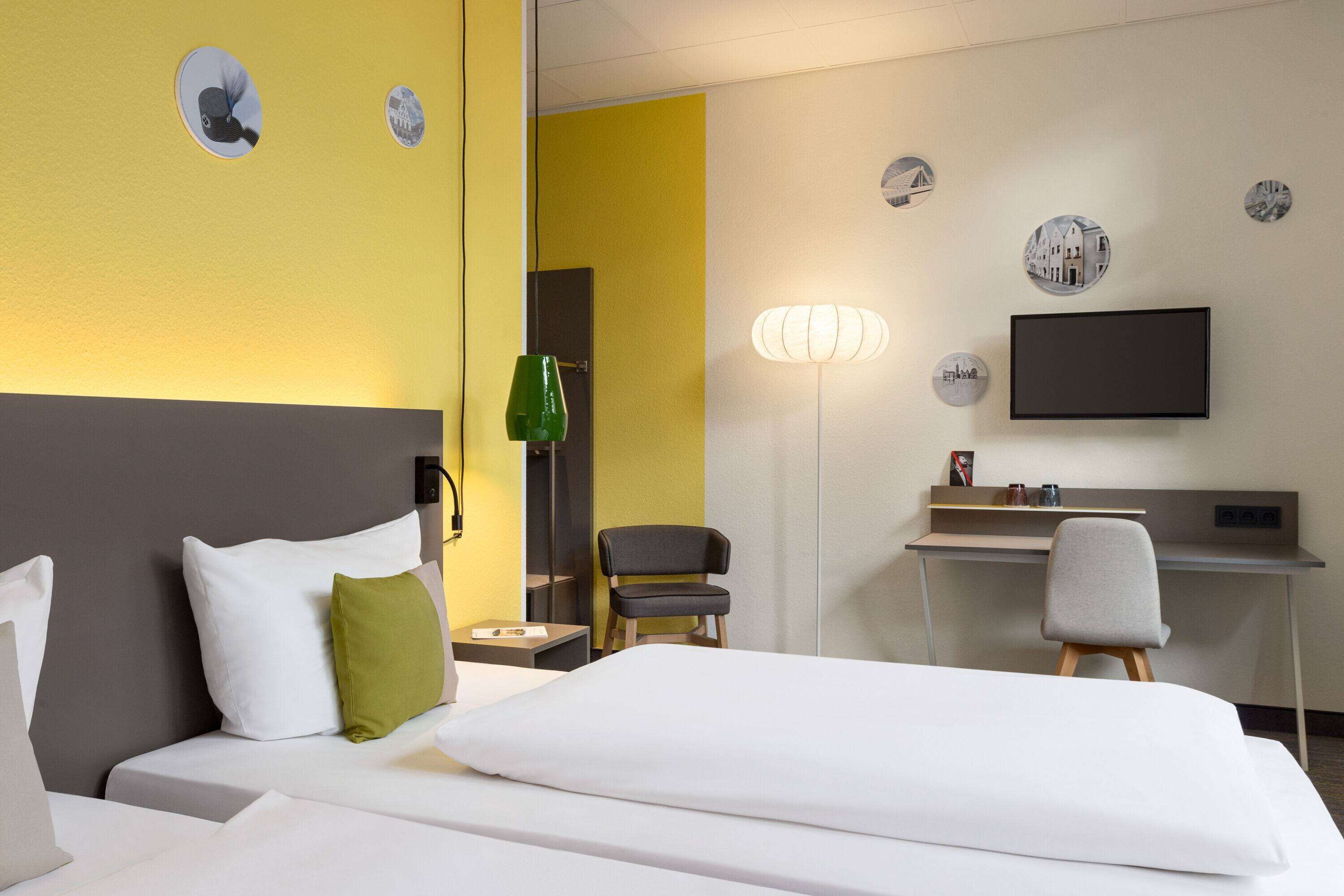 A hotel room with a bed, a desk, a chair, and a TV on the wall.