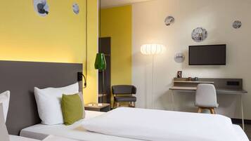 A hotel room with a bed, a desk, a chair, and a TV on the wall.