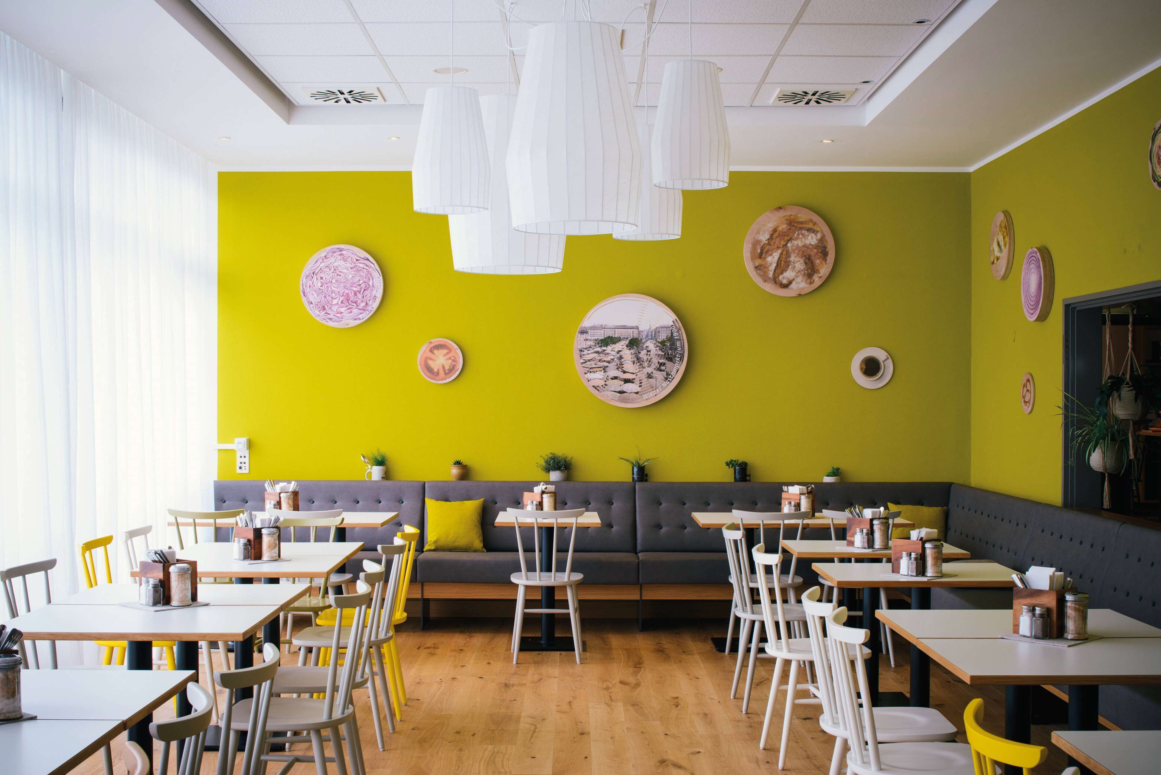 Een restaurant met houten tafels en stoelen, een groene wand met decoratieve borden en een grijze bank.
