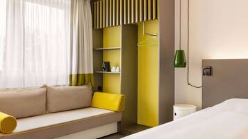 Una habitación de hotel con sofá, cama, mesita de noche, lámpara y armario.