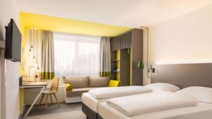 Quarto de hotel com cama, escrivaninha, cadeira, sofá e televisão.
