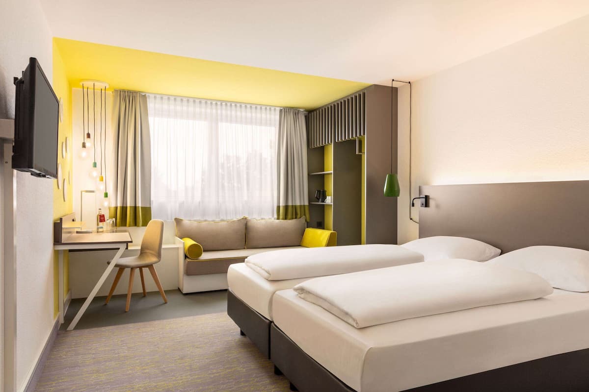 A hotel room with a bed, a desk, a chair, a sofa, and a TV.