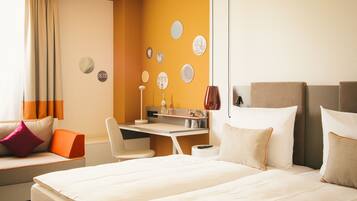 Habitación de hotel con cama, escritorio, silla y sofá. Decoración en las paredes y una ventana con cortinas.