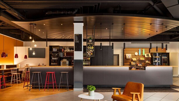 Uma área de bar moderna com banquetas, um balcão e um espaço de estar com uma cadeira e uma mesa.