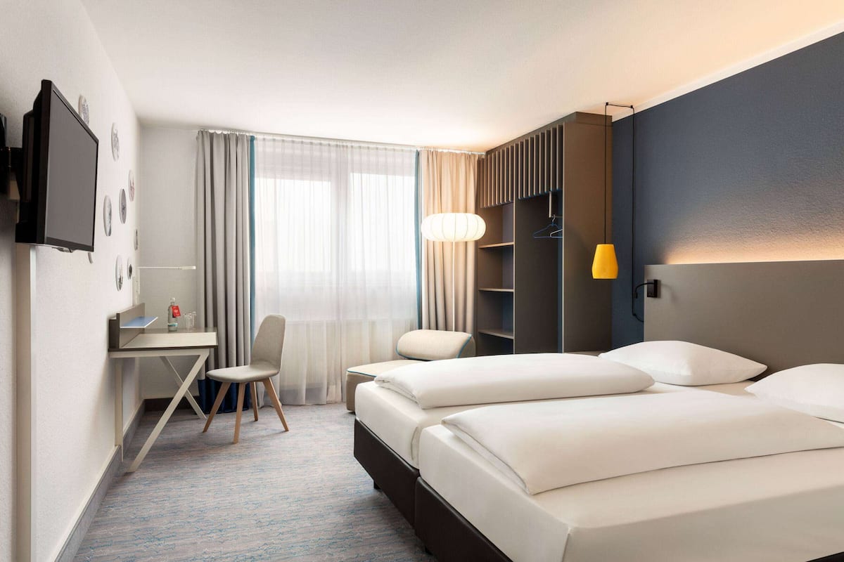 A hotel room with a bed, a desk, a chair, a TV, and a window with curtains.