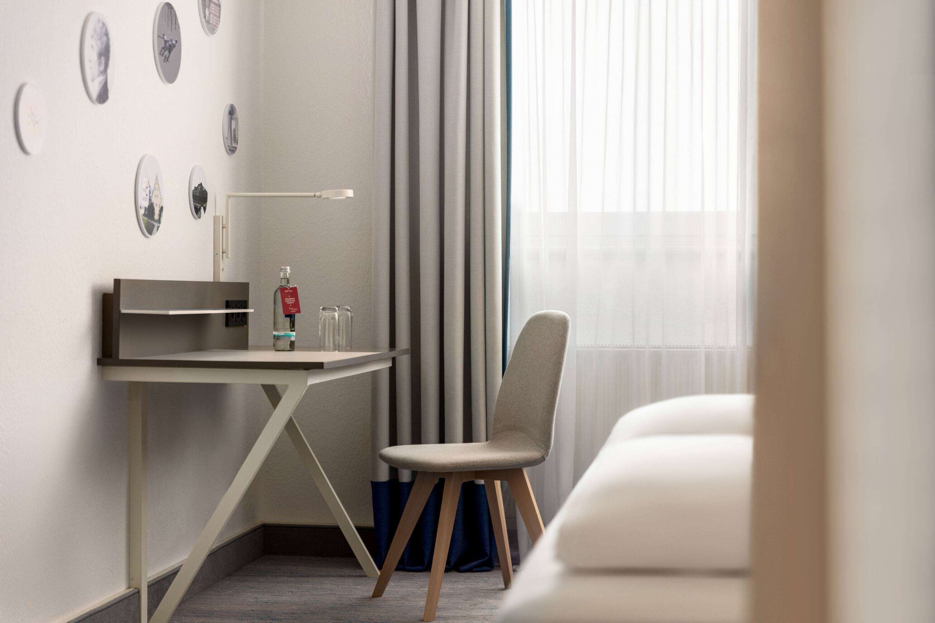 A modern hotel room with a desk, chair, and a bed.