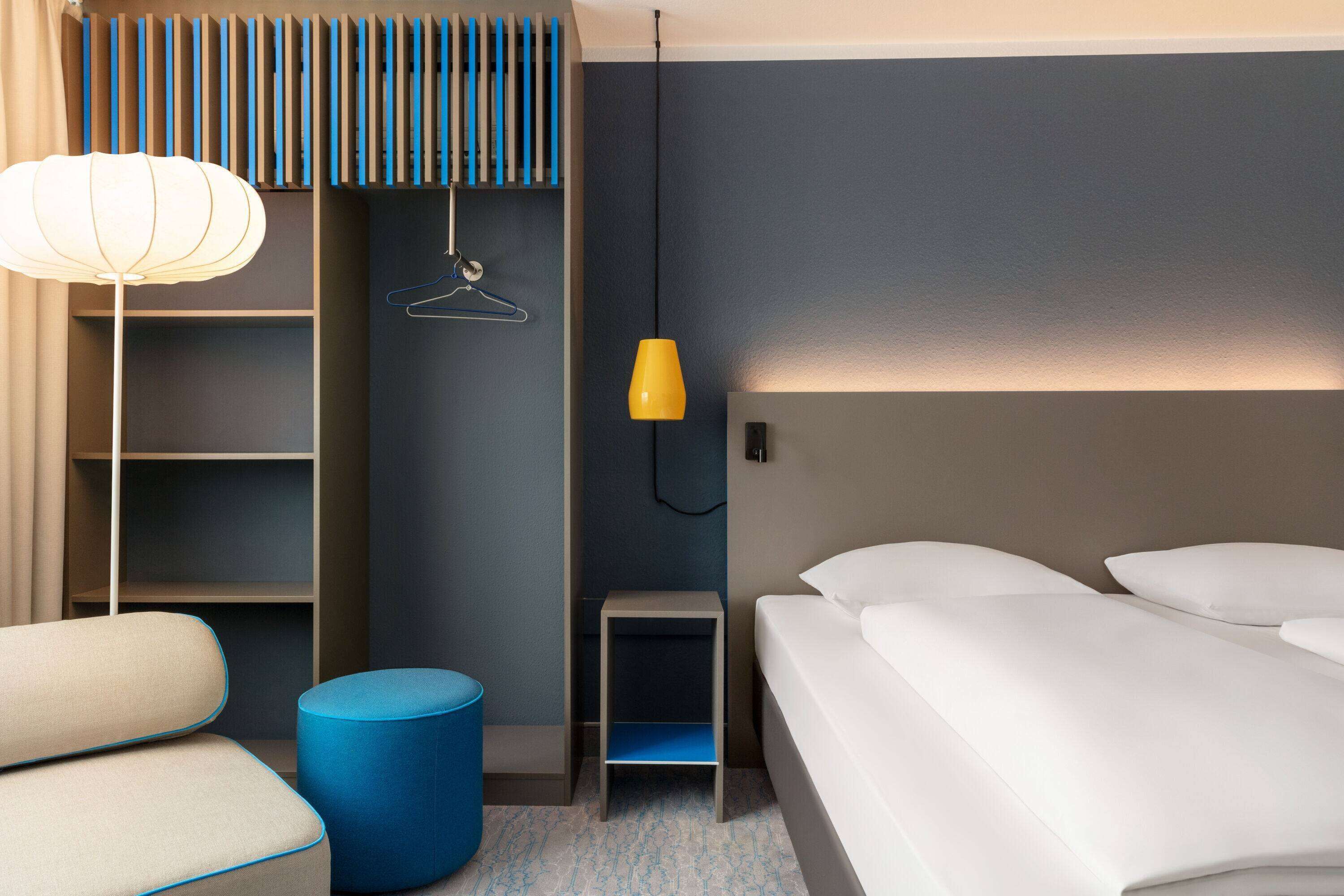 Una habitación de hotel moderna con una cama, una mesita de noche, una lámpara, un armario y un espacio para sentarse.
