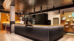 Uma área de recepção moderna com um balcão central, um espaço de bar com prateleiras e uma área de estar com bancos.